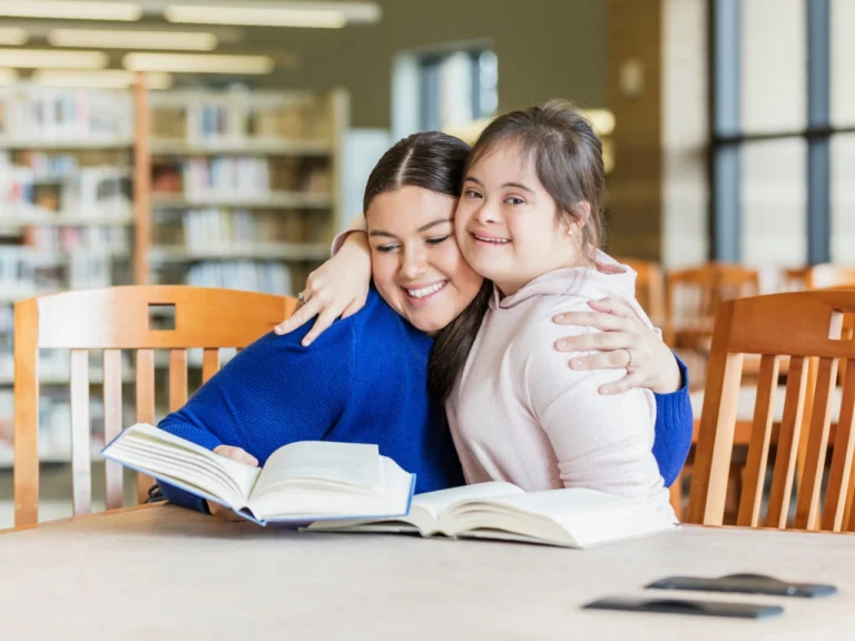 a female support worker hugging cheek to cheek with a beautiful girl with down syndrome